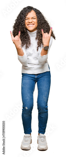 Young beautiful woman with curly hair wearing turtleneck sweater shouting with crazy expression doing rock symbol with hands up. Music star. Heavy concept.