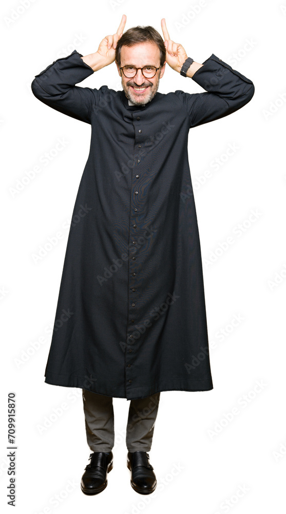 Middle age priest man wearing catholic robe Posing funny and crazy with fingers on head as bunny ears, smiling cheerful Middle age priest man wearing catholic robe Posing funny and crazy with fingers on head as bunny ears, smiling cheerful