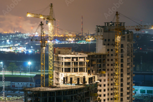 Construction site at night. Cranes working at night over an unfinished house in the light of lanterns. The concept of buying a home on credit, mortgage housing. © Pokoman