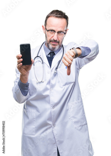 Middle age senior hoary doctor man showing smartphone screen over isolated background with angry face, negative sign showing dislike with thumbs down, rejection concept © Krakenimages.com