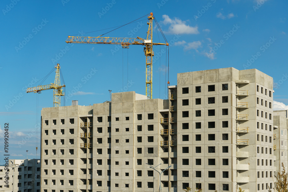Silhouettes of working construction cranes against the background of an unfinished residential building. Multi-storey luxury apartment building on a construction site Silhouettes of working construction cranes against the background of an unfinished residential building. Multi-storey luxury apartment building on a construction site