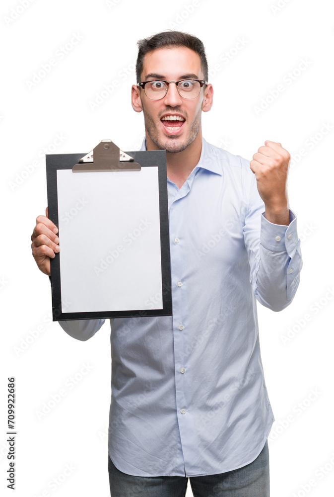 Handsome young business man showing a clipboard screaming proud and celebrating victory and success very excited, cheering emotion Handsome young business man showing a clipboard screaming proud and celebrating victory and success very excited, cheering emotion