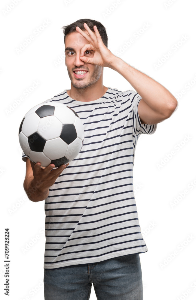 Handsome young man holding soccer football with happy face smiling doing ok sign with hand on eye looking through fingers Handsome young man holding soccer football with happy face smiling doing ok sign with hand on eye looking through fingers