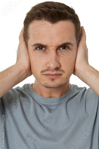 caucasian man in t-shirt covers ears with hands on white background
