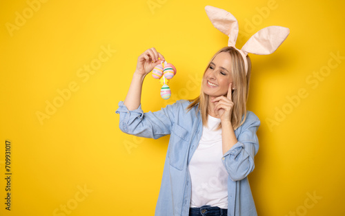 Young smiling positive fun cheerful woman wearing casual clothes bunny rabbit ears hold wicker basket show colorful egg isolated on yellow background studio portrait. Happy Easter concept