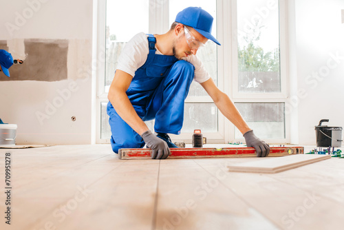Close up hands of repairman in grey gloves and special uniform laying tiles with tile leveling system on the floor in a new house 