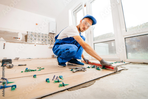 Close up hands of repairman in grey gloves and special uniform laying tiles with tile leveling system on the floor in a new house 