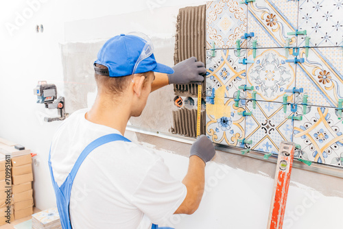 Adult repairman in a special uniform laying tiles on the wall at bathroom in new house 