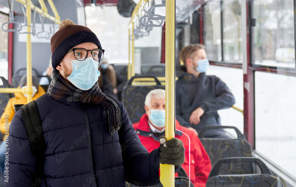 custom made wallpaper toronto digitalClose up of pensive adult male wearing winter clothes standing looking at window in transport. Crop of young man in protective mask and passengers sitting behind in moving bus. Concept of city life.