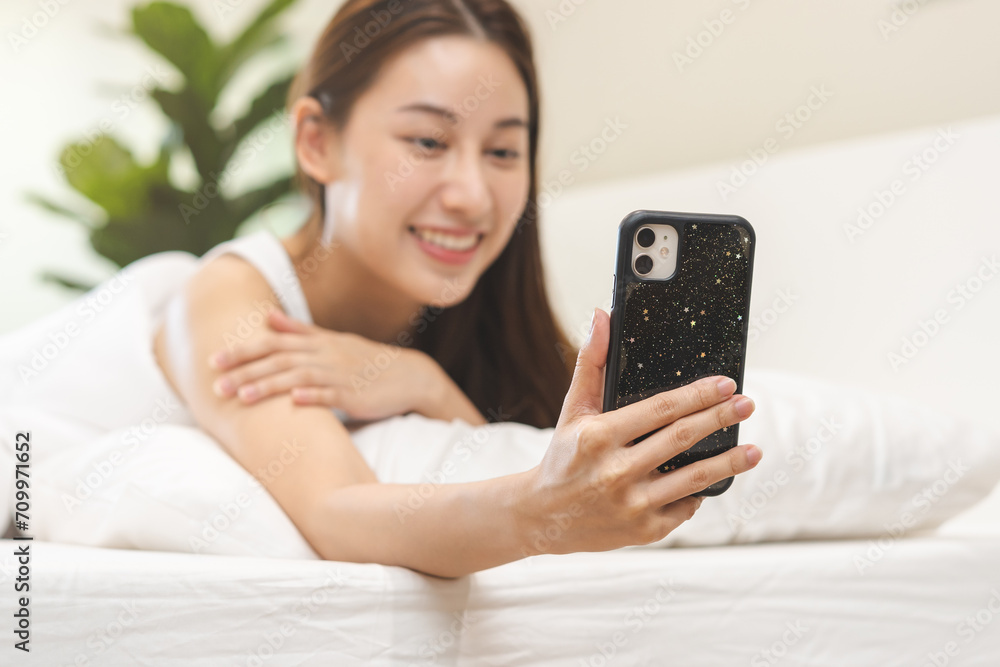 Attractive smile pretty asian young woman using and playing mobile phone, smartphone have video call or chat, lying down relax in bedroom wake up with covered blanket in cozy white bed in the morning Attractive smile pretty asian young woman using and playing mobile phone, smartphone have video call or chat, lying down relax in bedroom wake up with covered blanket in cozy white bed in the morning