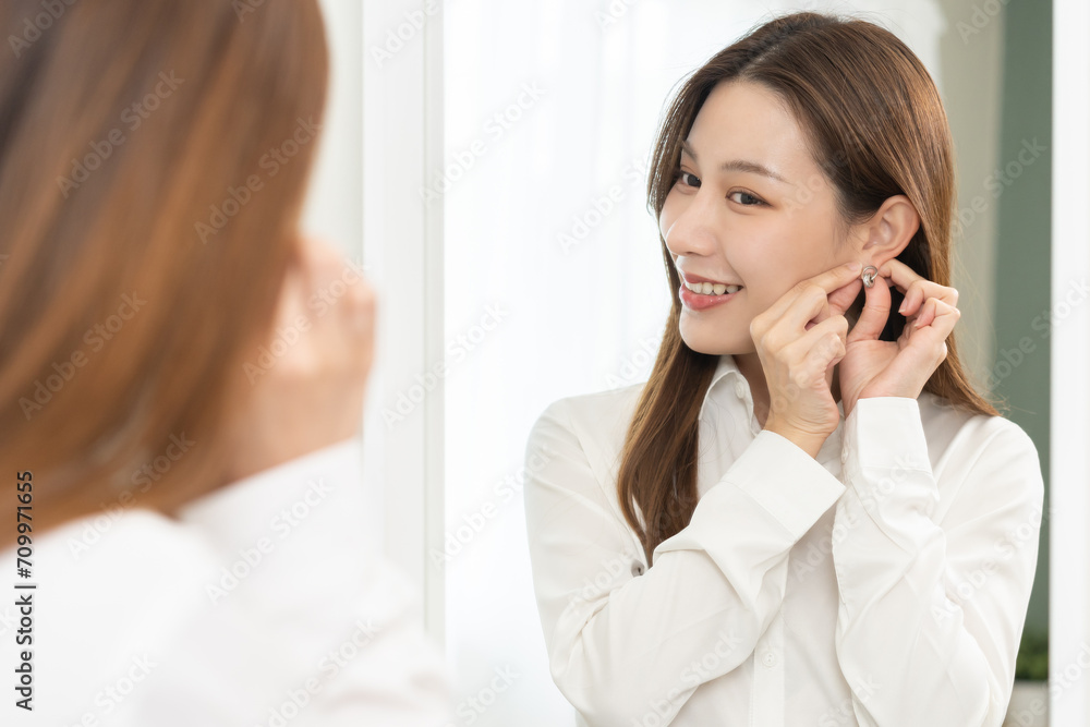 Get dress, pretty asian young woman, businesswoman standing putting earring or jewelry, wearing white shirt formal getting dressed getting ready before go to work looking reflection the mirror at home Get dress, pretty asian young woman, businesswoman standing putting earring or jewelry, wearing white shirt formal getting dressed getting ready before go to work looking reflection the mirror at home