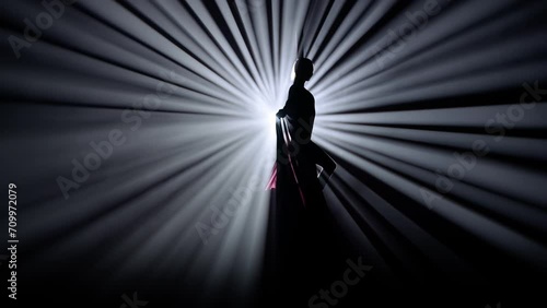 Silhouette of female isolated on black background against bright spotlight. Girl aerial dancer performs element on air silk. photo