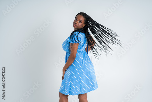 Plus size female model posing in blue dress on white background, young African woman with curvy figure and pigtailed hairstyle, afro braids photo