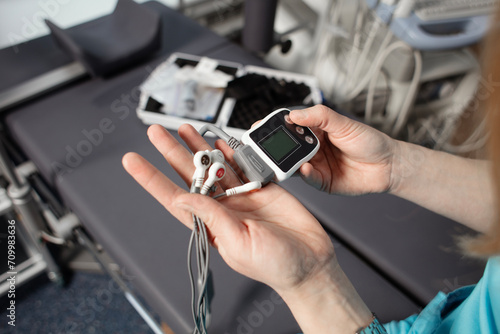Doctor showing ECG holter monitor to patient in pediatric clinic. Holter monitoring device in a doctor hands before a diagnostic. Preparation for a heart rhythm diagnistic. Professional medicine.