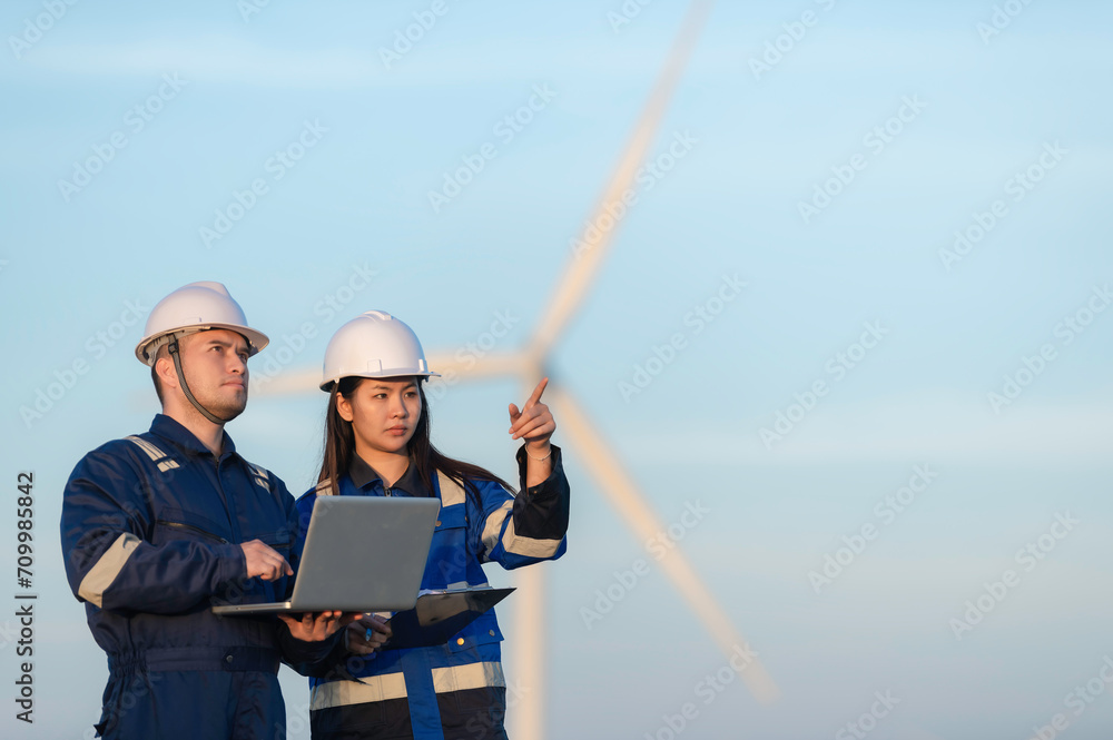 Two engineers working and holding the report at wind turbine farm Power Generator Station on mountain,Thailand people,Technician man and woman discuss about work Two engineers working and holding the report at wind turbine farm Power Generator Station on mountain,Thailand people,Technician man and woman discuss about work
