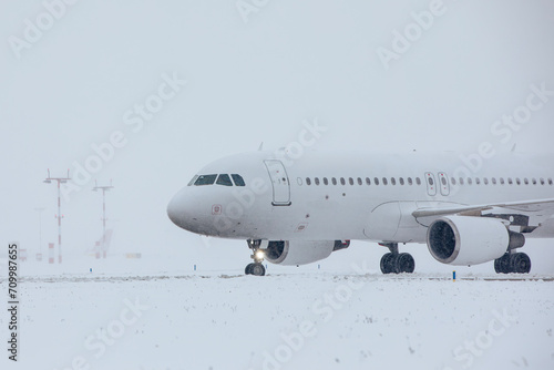 Traffic at airport during snowfall. Passenger airplane taxiing to runway for take off on frosty winter day..