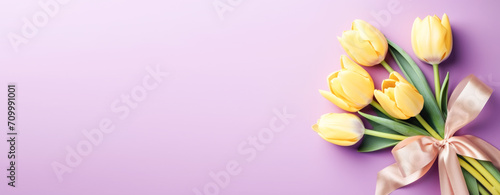 Beautiful flowers, yellow tulips tied with a satin ribbon, pastel pink lilac background. Spring floral background