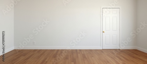 An unfurnished room with white walls, wood flooring, and a corner door. photo