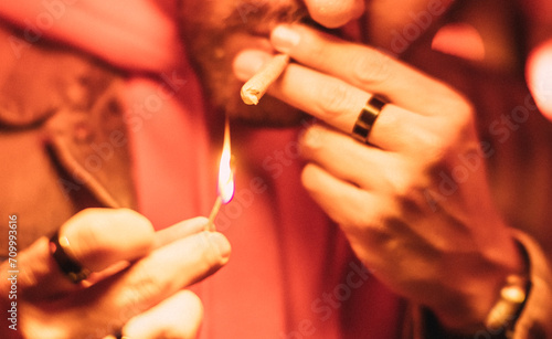 Detail of a man's hands lighting a marijuana cigarette under a red light.