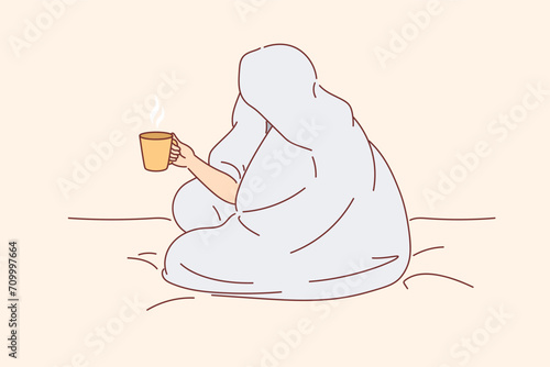 Man drinks coffee sitting on bed and wrapped in blanket to warm up after walk along winter street