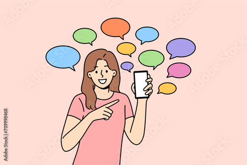 Woman shows off messages pointing fingers at phone and calling for downloading new mobile messenger. Girl smiles standing among dialogue clouds symbolizing exchange of messages on social networks.