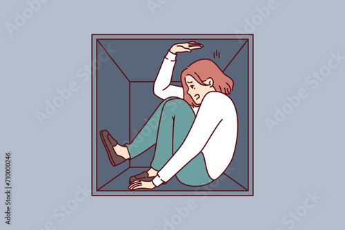 Woman suffering from claustrophobia sits in cramped box and feels pressure of walls, as metaphor for cramped housing. Girl experiences problems due to claustrophobia and fear of closed spaces.