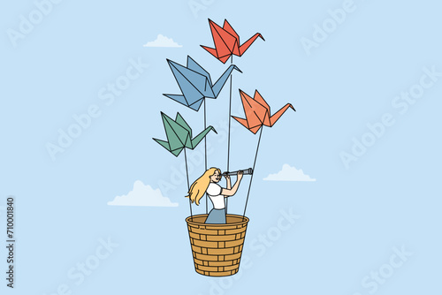 Woman travel flying in basket of origami swans and exploring world with spyglass. Girl dreams of travel and adventure, fantasizing about possibility of fly across sky on paper birds.