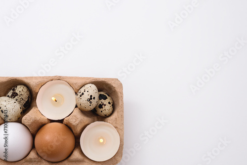 Eggs and candle in eggshell in tray on white background. Quail and chicken eggs. Copy space. Easter holiday concept