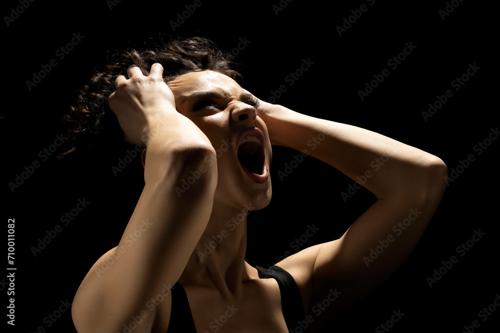 Portrait of a screaming woman in the shadow, hold her head , closed eyes on a black background Portrait of a screaming woman in the shadow, hold her head , closed eyes on a black background