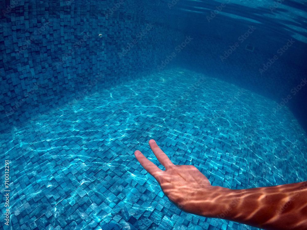 mão fazendo sinal de paz em água de piscina 