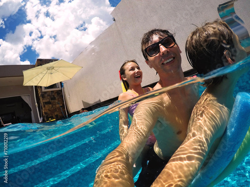 pai brincando com filhos em água de piscina, férias de verão  photo