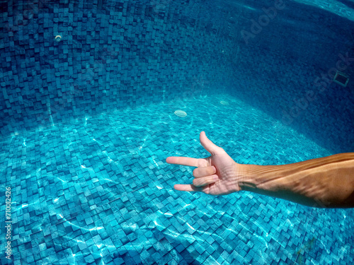 mão fazendo sinal de eu te amo em água de piscina  photo