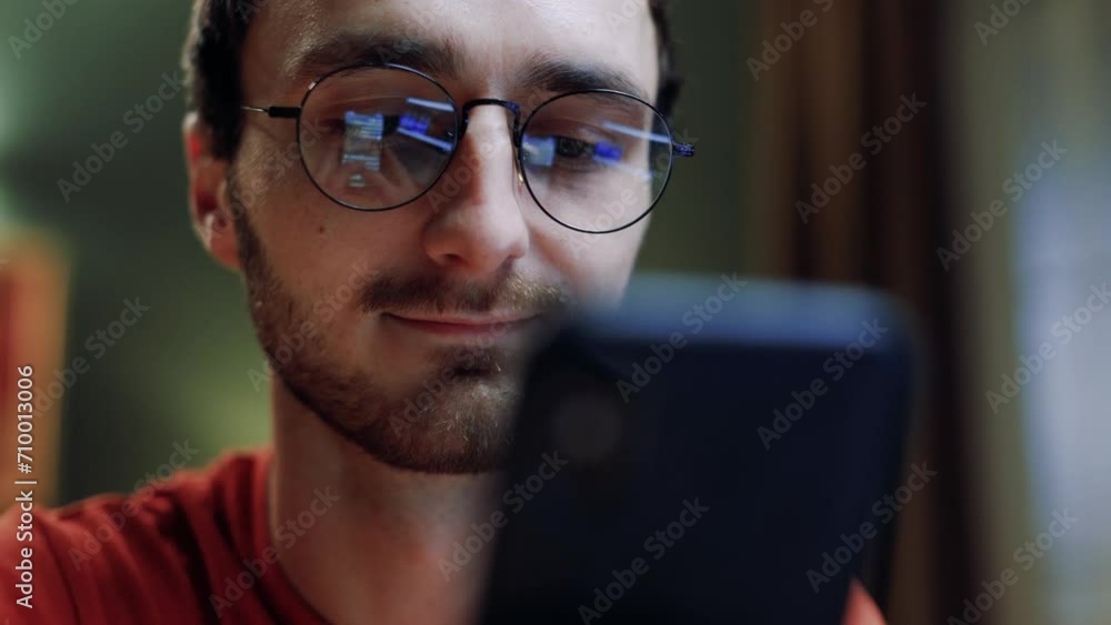 Young guy holding smartphone. Satisfied man looking at gadget screen. Male wearing glasses. Smiling man using phone for typing message. Male communicating with colleague or friend online. Young guy holding smartphone. Satisfied man looking at gadget screen. Male wearing glasses. Smiling man using phone for typing message. Male communicating with colleague or friend online.