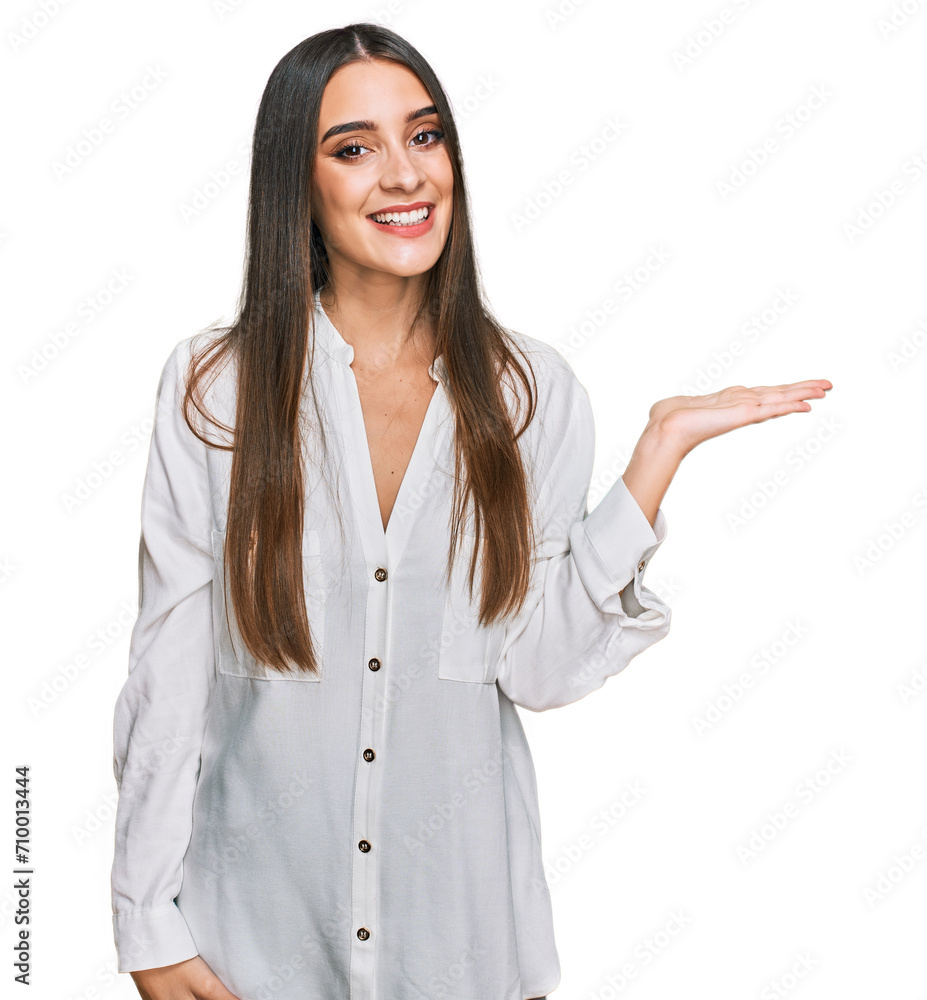 Young beautiful woman wearing casual white shirt smiling cheerful presenting and pointing with palm of hand looking at the camera. Young beautiful woman wearing casual white shirt smiling cheerful presenting and pointing with palm of hand looking at the camera.
