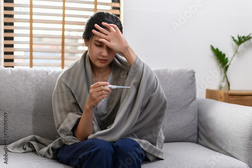 Young Asian woman have a cold and high fever while checking body temperature by using digital thermometer. Daily lifestyle health care concept.