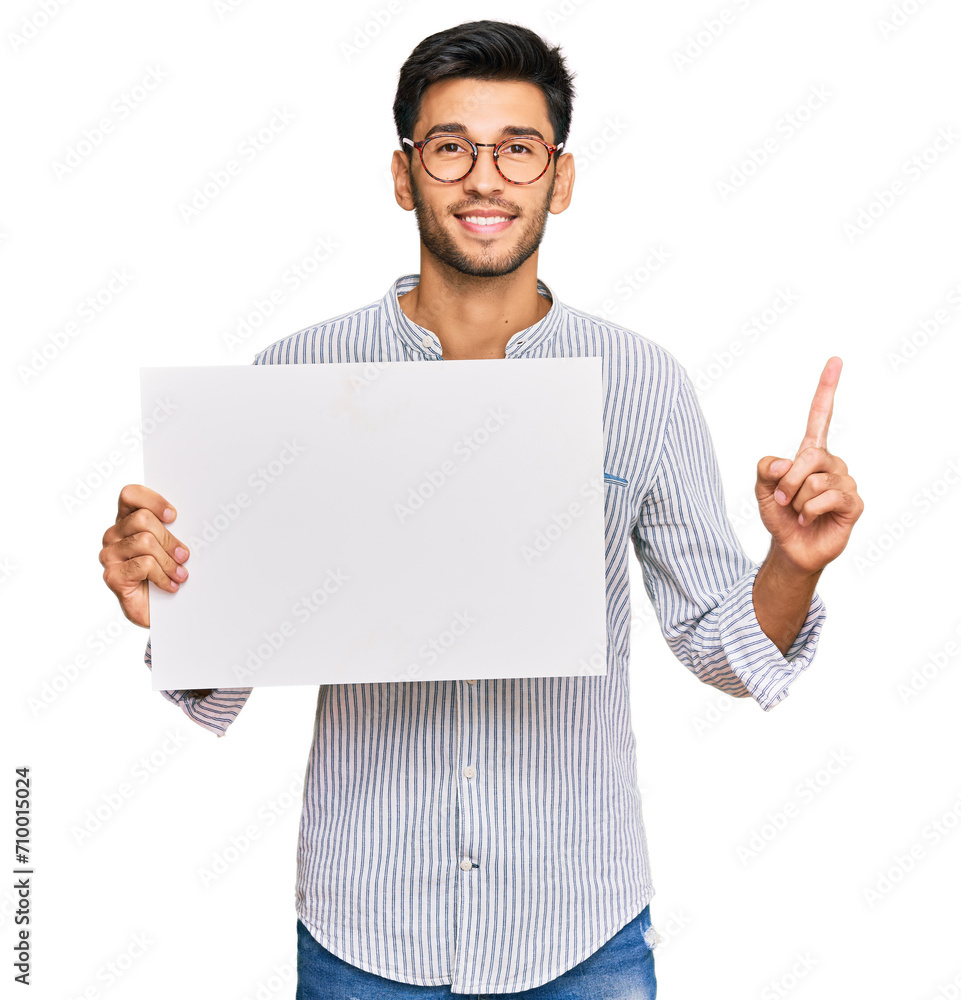 Young handsome man holding blank empty banner surprised with an idea or question pointing finger with happy face, number one Young handsome man holding blank empty banner surprised with an idea or question pointing finger with happy face, number one