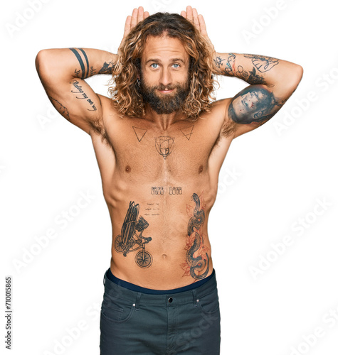 Handsome man with beard and long hair standing shirtless showing tattoos doing bunny ears gesture with hands palms looking cynical and skeptical. easter rabbit concept. photo