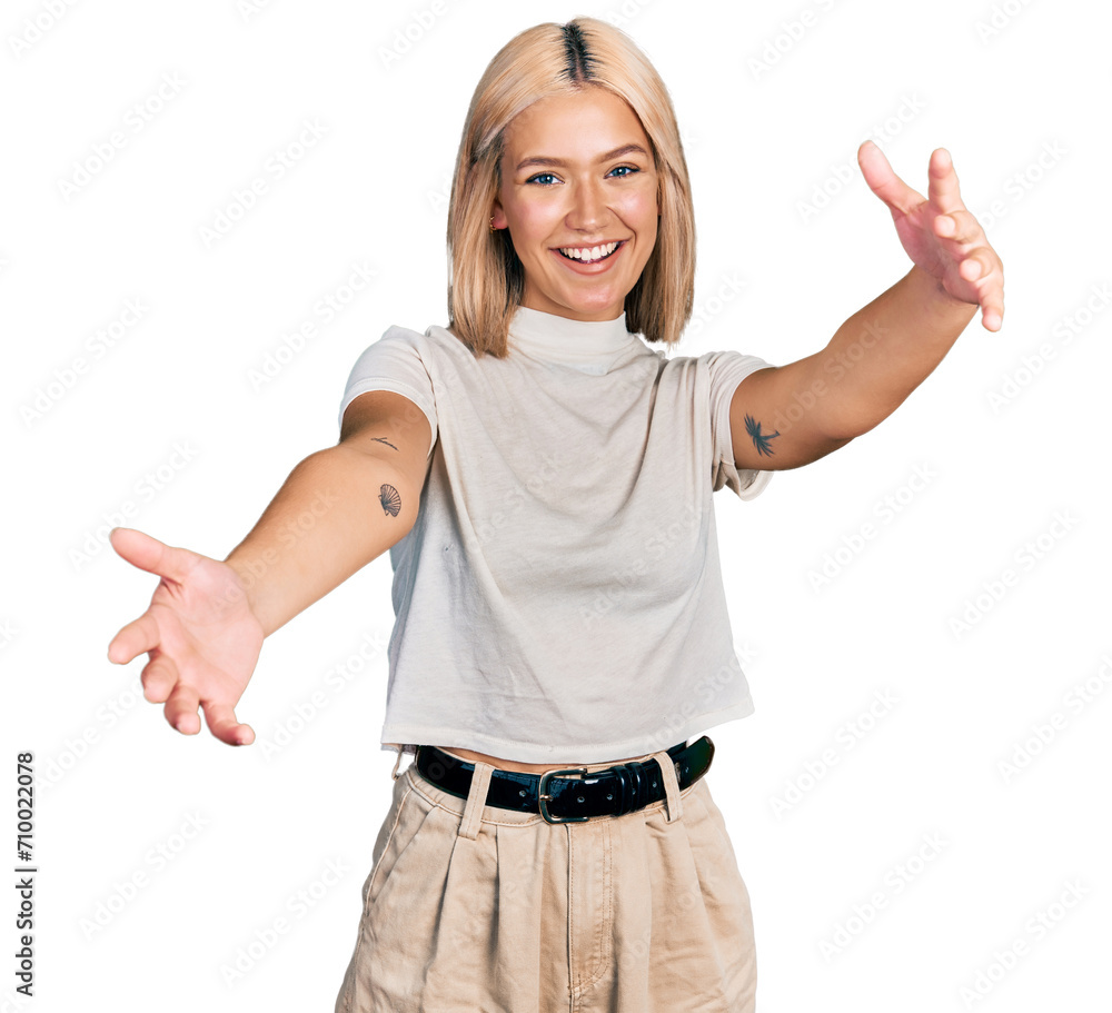 Beautiful young blonde woman wearing casual white t shirt looking at the camera smiling with open arms for hug. cheerful expression embracing happiness.