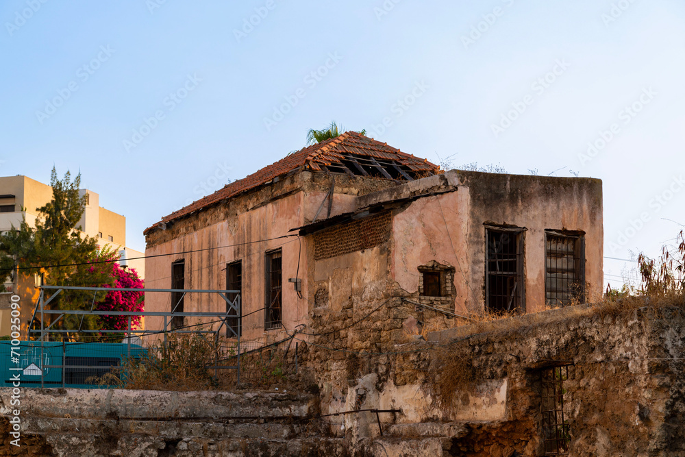 Old, worn building with a damaged roof in Neve Shannan, south Tel Aviv, surrounded by urban decay and vibrant flora, reflecting a stark socio-cultural contrast