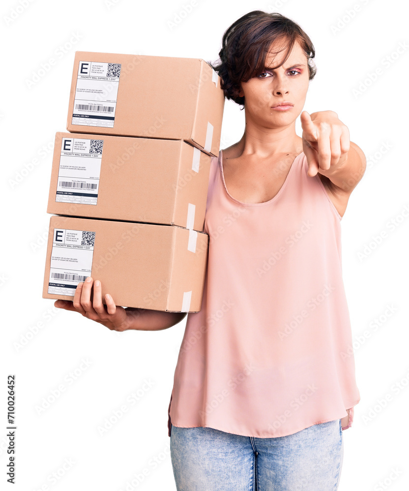 Beautiful young woman with short hair holding delivery packages pointing with finger to the camera and to you, confident gesture looking serious Beautiful young woman with short hair holding delivery packages pointing with finger to the camera and to you, confident gesture looking serious
