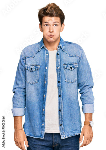 Handsome caucasian man wearing casual denim jacket puffing cheeks with funny face. mouth inflated with air, crazy expression.