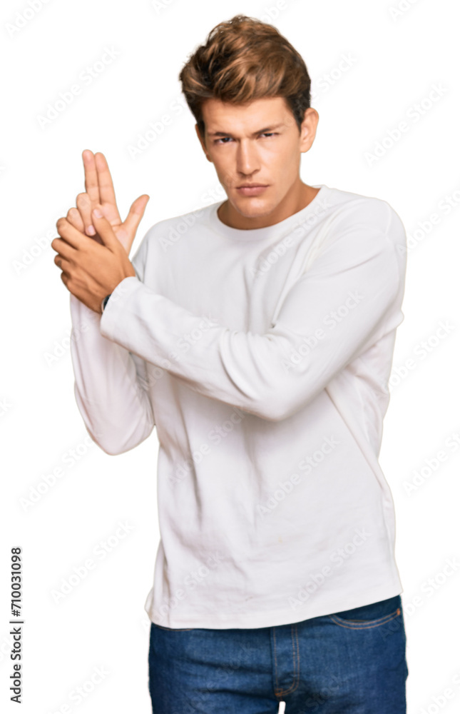 Handsome caucasian man wearing casual white sweater holding symbolic gun with hand gesture, playing killing shooting weapons, angry face Handsome caucasian man wearing casual white sweater holding symbolic gun with hand gesture, playing killing shooting weapons, angry face