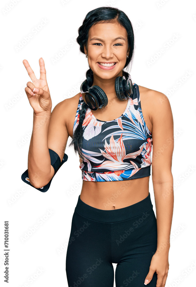 Beautiful hispanic woman wearing sportswear and headphones showing and pointing up with fingers number two while smiling confident and happy. Beautiful hispanic woman wearing sportswear and headphones showing and pointing up with fingers number two while smiling confident and happy.