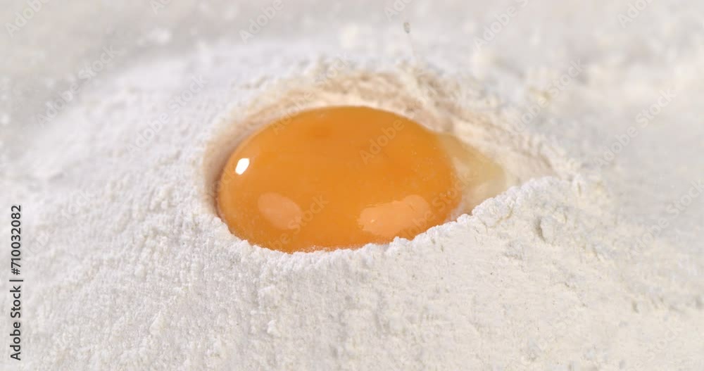 Super slow motion macro of fresh egg yolk is put in flour by artisan baker chef for preparation a dough while making homemade bread, pasta or pizza in traditional bakery kitchen. Super slow motion macro of fresh egg yolk is put in flour by artisan baker chef for preparation a dough while making homemade bread, pasta or pizza in traditional bakery kitchen.