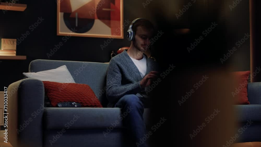 Young man sitting on couch and holding tablet. Male relaxing at home. Male wearing headphones. Young guy listening music. Man sitting on sofa and using devices. Student working or studying at home. Young man sitting on couch and holding tablet. Male relaxing at home. Male wearing headphones. Young guy listening music. Man sitting on sofa and using devices. Student working or studying at home.