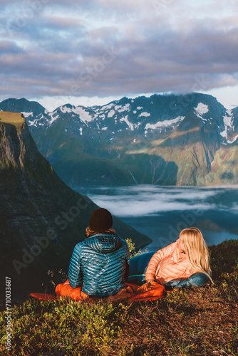 Romantic couple in sleeping bags on bivouac travel in Norway mountains with camping travel gear. Friends hiking enjoying fjord view, active vacations healthy lifestyle outdoor Valentines day holiday