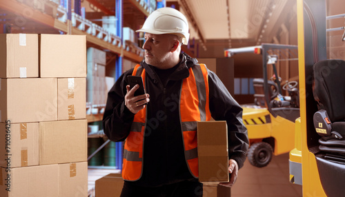 Man warehouse contractor. Factory storage manager. Product storage area. Clipboard man thought. Warehouse contractor inspects goods. Tiered racks with boxes behind guy. Logistics, fulfillment