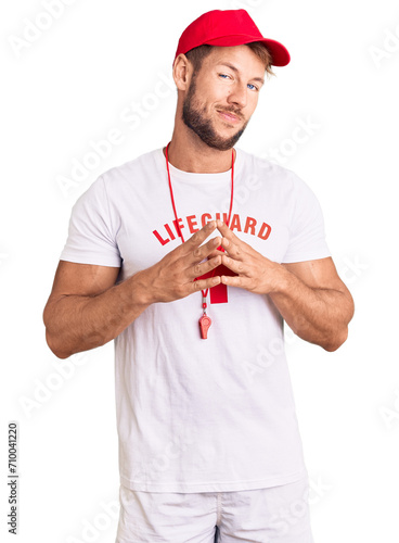 Young caucasian man wearing lifeguard t shirt holding whistle hands together and fingers crossed smiling relaxed and cheerful. success and optimistic
