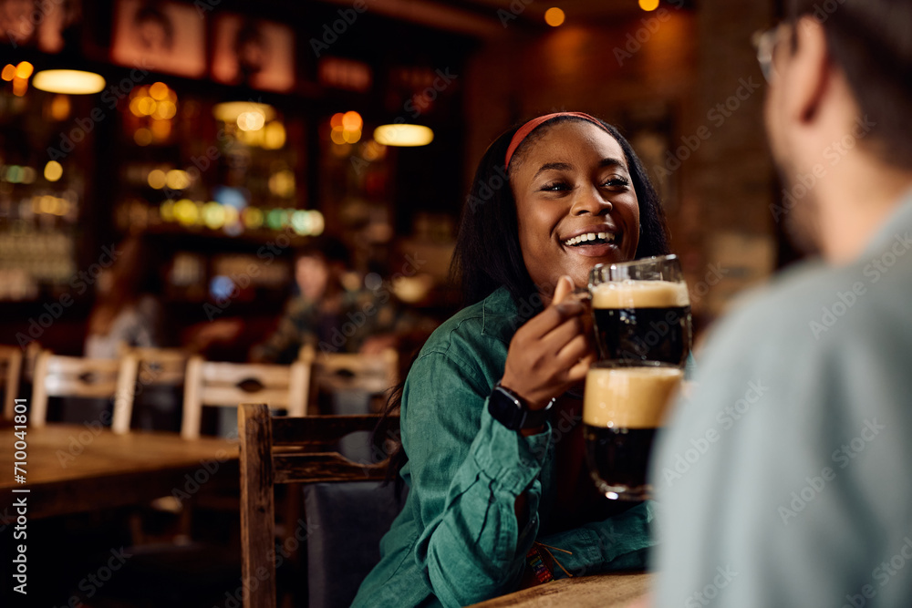 Happy black woman and her friend toasting with beer in pub.