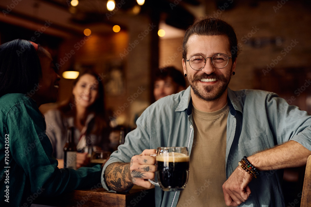 Happy man enjoying in glass of beer with his friends in bar and looking at camera.